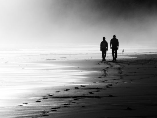 Two men walking on a beach, black and white photo.